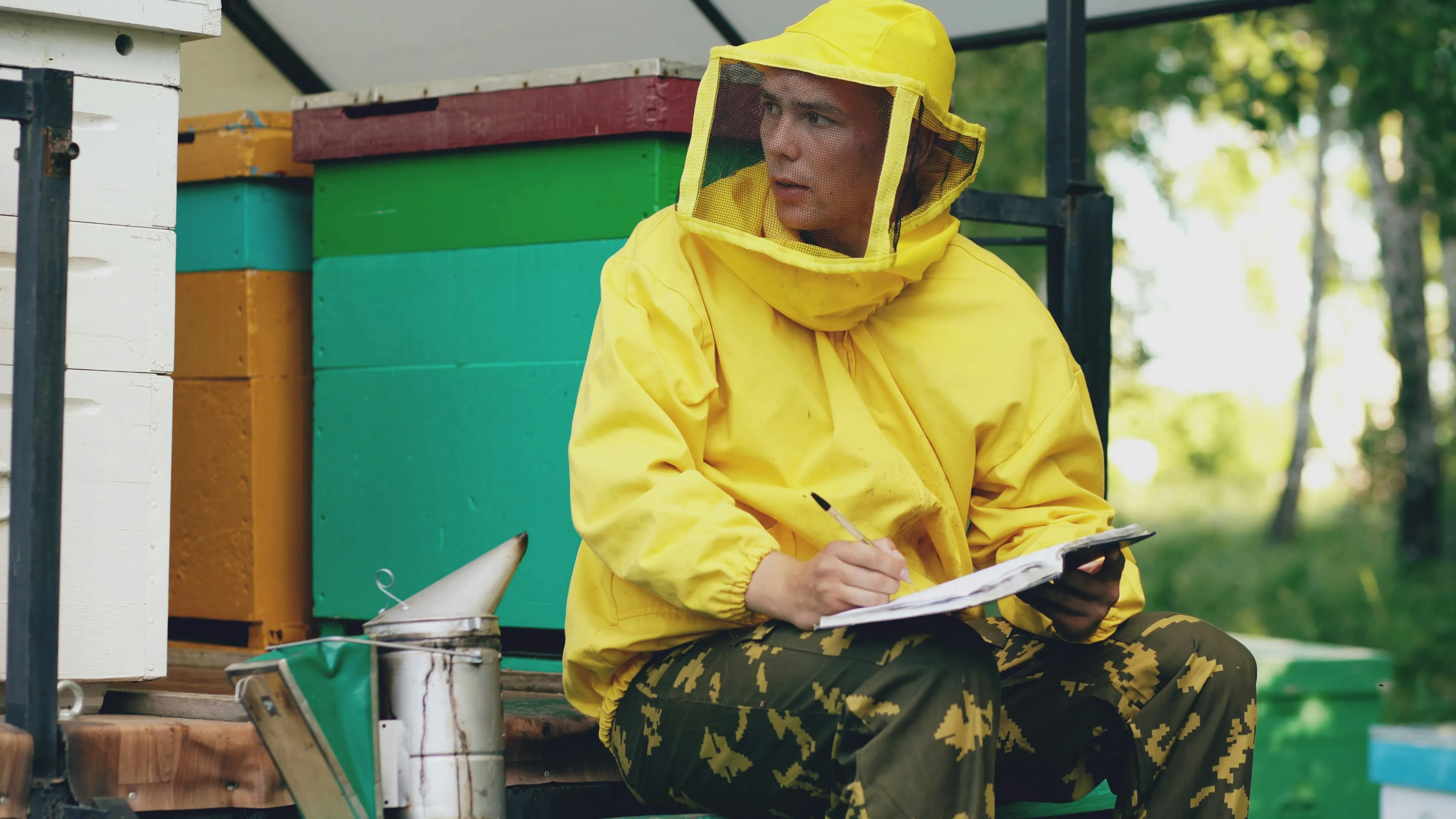 Beekeeper in protective suit writing notes near beehives on a sunny day